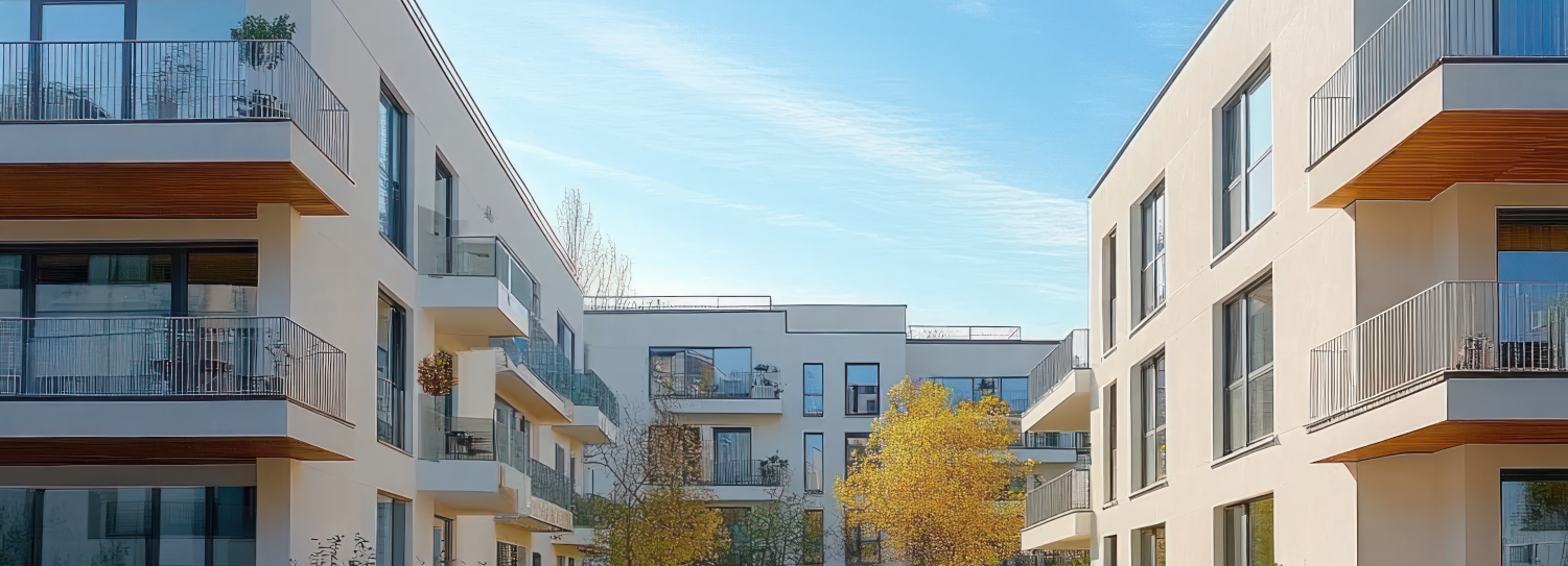 Moderne Wohngebäude mit Balkonen und einem Baum im Innenhof unter blauem Himmel.